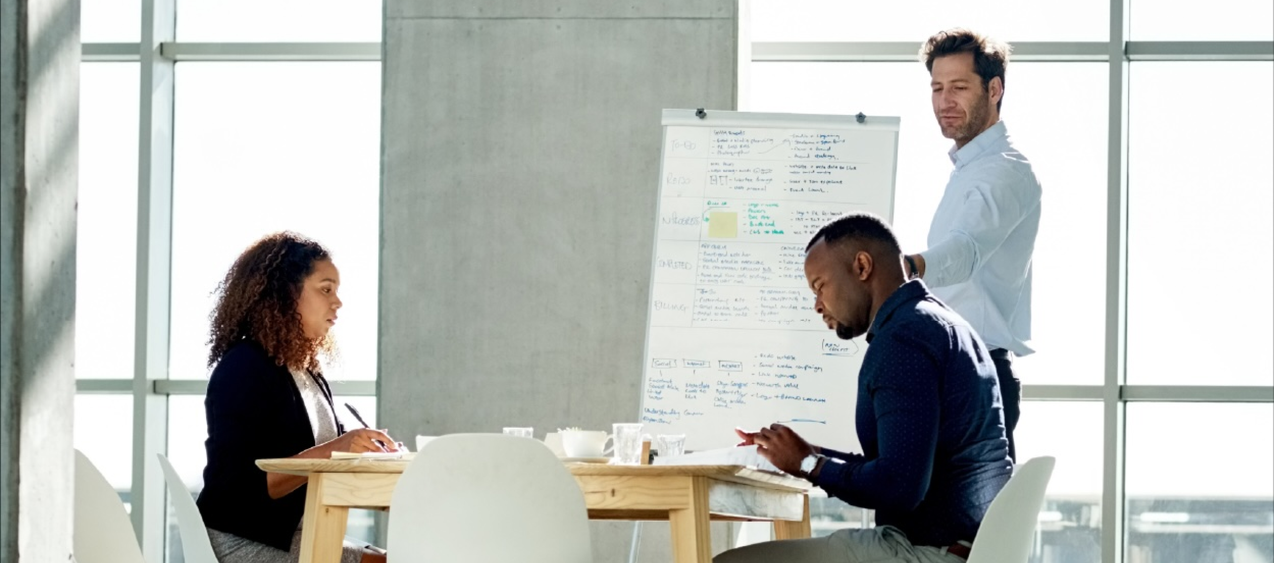 Coworkers in discussion in a meeting room with a whiteboard and a table 