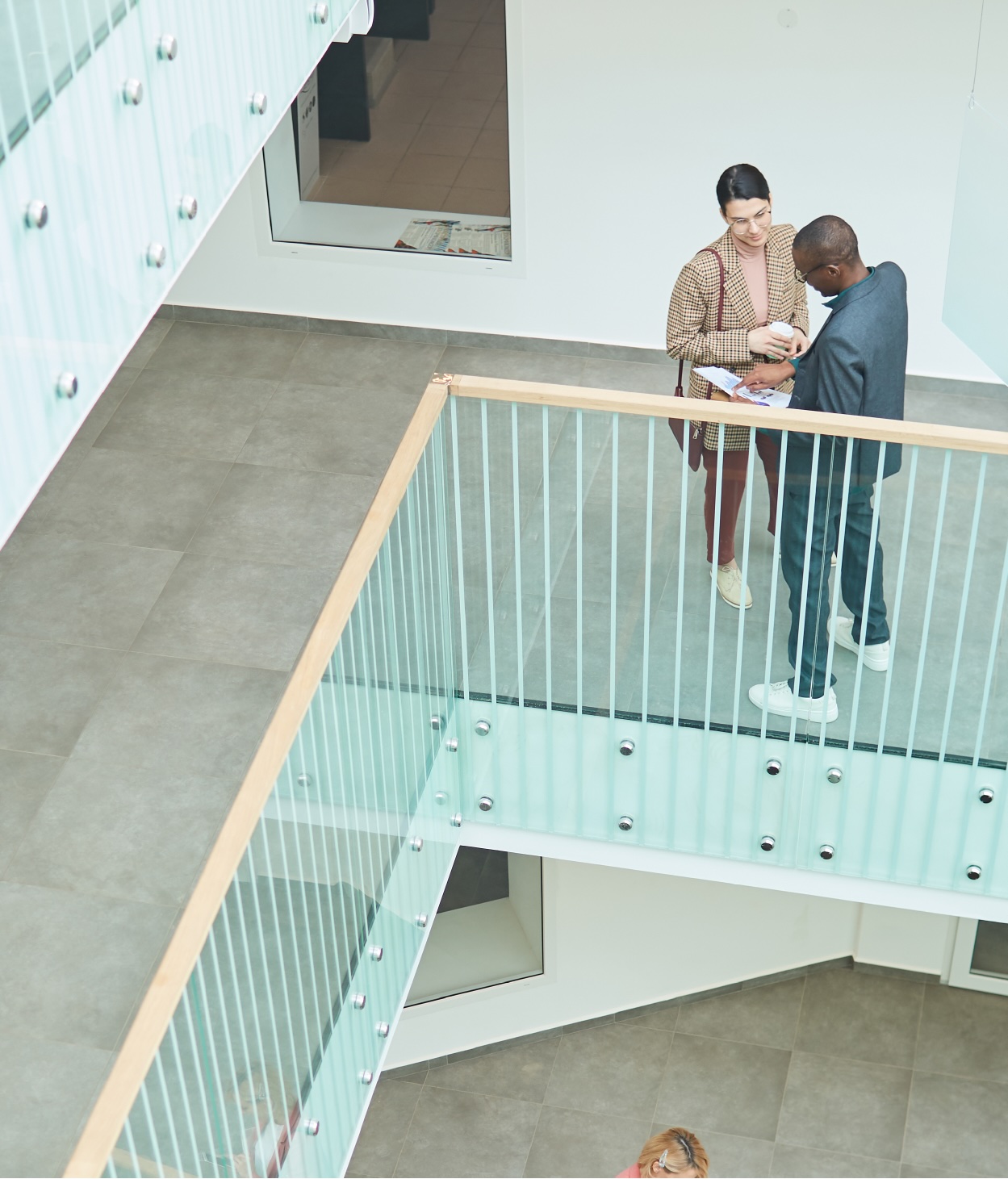 Two people in business attire discuss a project on an indoor office balcony